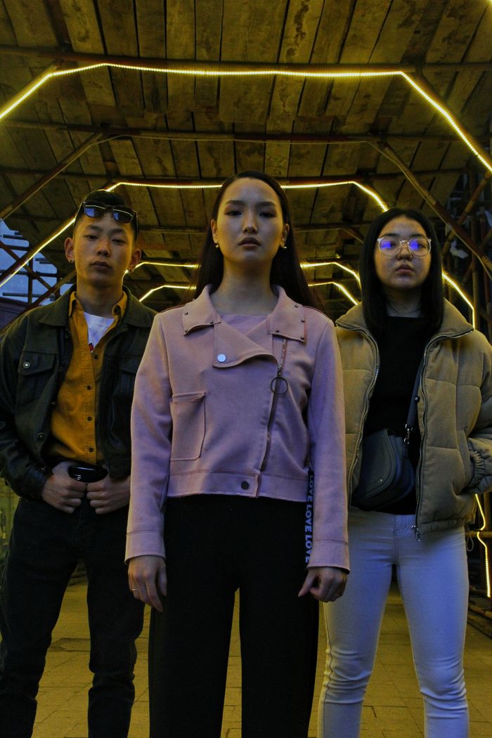 From below of young Asian friends in stylish clothes standing on street under roof with bright illumination