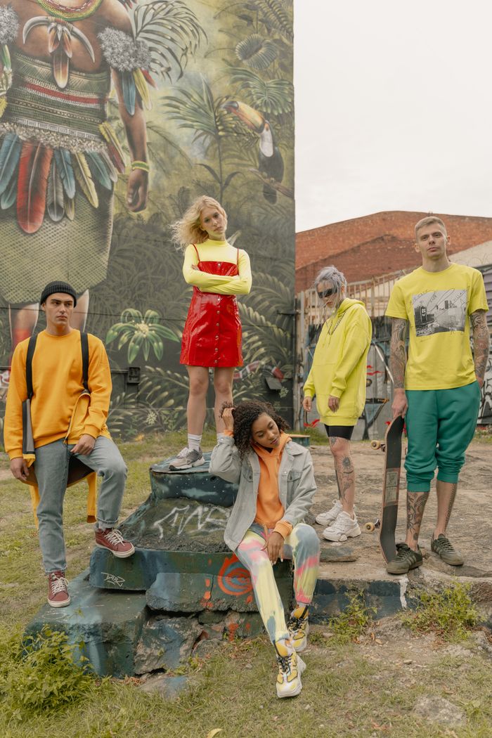 A fashionable group of young adults posing beside a vibrant street art mural, showcasing street style and creativity.