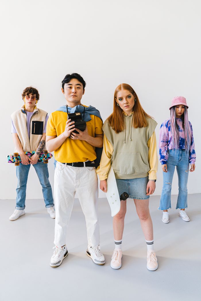 A group of stylish friends posing indoors with skateboards and a camera.