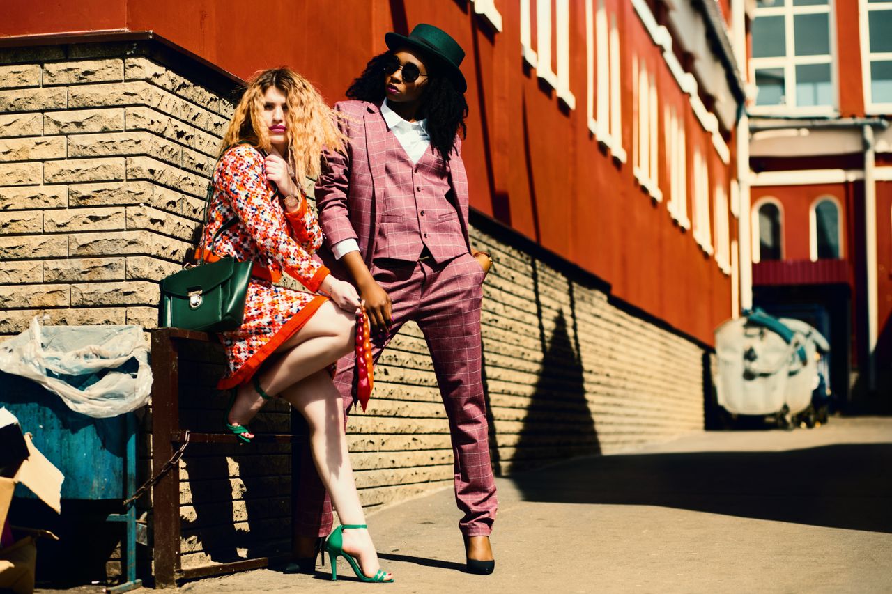 Fashionable duo posing outdoors in vibrant outfits, embracing urban style and confidence.