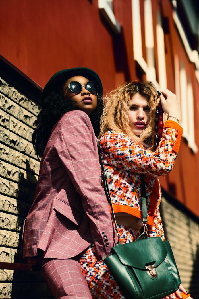 Two fashionable women posing stylishly against an urban background, showcasing vibrant outfits and accessories.